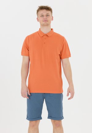 Orange polo shirt med en treknaps placket, korte ærmer og et diskret logo; parret med opsmøgede blå shorts.