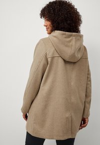 Beige wollenblendjas met een capuchon, met een ontspannen pasvorm, textiel stof en stiksels op de schouders. Lange mouwen en een middellange snit.