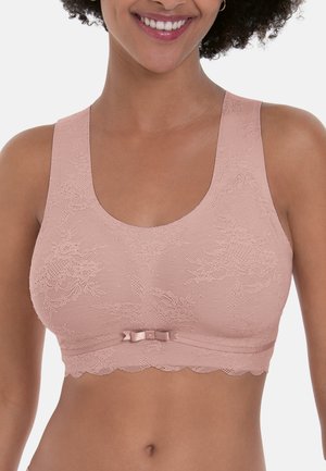 Vrouw die lacht en een lichtroze kanten bralette draagt met brede bandjes en een klein strikje middenvoor.