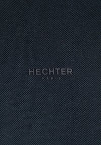 Schwarzer, strukturierten Stoff mit einem subtilen Webmuster und einem embossed "HECHTER PARIS"-Logo in der Mitte.