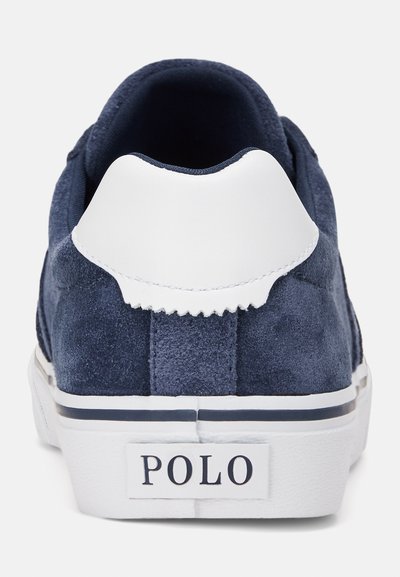 Marineblå ruskinds sneakers med en hvid læderheel-tab, tekstureret overdel og en hvid gummisål med en marineblå stribe og "POLO" logo.