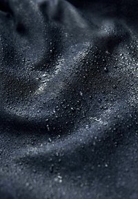 Tessuto nero con una superficie morbida, che mostra gocce d'acqua sulla sua superficie, creando un aspetto lucido con pieghe leggere.