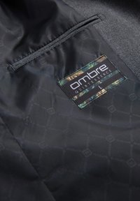 Schwarzes Stoffinterieur mit einem gesteppten Muster, ausgestattet mit einem kleinen Camouflage-Etikett mit der Aufschrift "ombre QUINTESSENCE L" und einer Reißverschlusstasche.