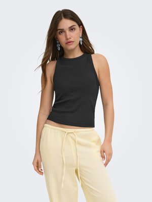Jeune femme aux longs cheveux bruns portant un haut noir sans manches, un pantalon jaune clair à cordon et des boucles d'oreilles bleues pendantes.