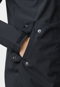 Black jacket featuring a textured material, snap and Velcro closures, with a side pocket opening for hand access.
