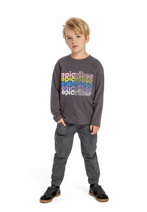 Grijze langemouwen shirt met meerkleurige tekst "epic vibes". Donkergrijze cargo broek met elastische boorden. Zwarte schoenen met een bruine zool.