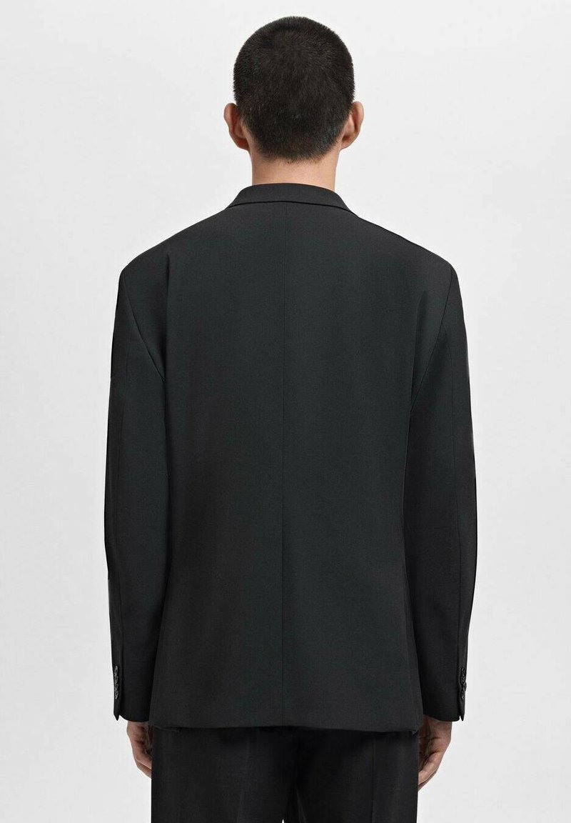 Blazer negro con un corte ajustado, hombros estructurados y cierre de un solo botón. Textura suave, brillo sutil y puños de dos botones.