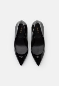 Escarpins en cuir verni noir avec un bout pointu, texture lisse et semelle rembourrée. Marque visible à l'intérieur des chaussures.