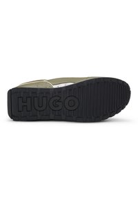 Černá gumová podrážka tenisky s texturovanými drážkami a zvýšeným logem "HUGO"; vrchní část v olivově zelené barvě s béžovými akcenty a perforacemi.