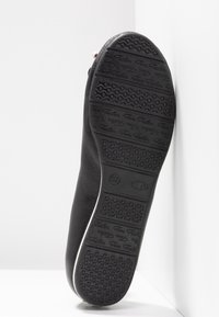 Semelle de chaussure noire avec motif sur la bande de roulement, avec le nom de la marque "Tom Tailor" et la taille "37" embossés sous la semelle.