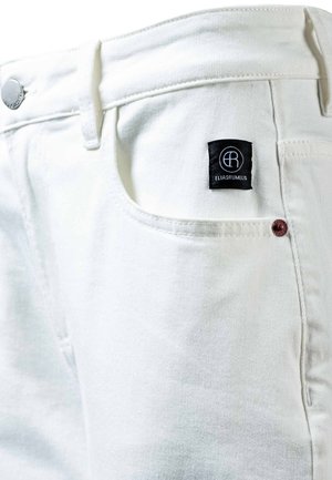 Białe jeansy z denimu, zbliżenie na przednią kieszeń, srebrny guzik oraz czarną metkę marki z białym logo i napisem "ELIASRUMELIS".