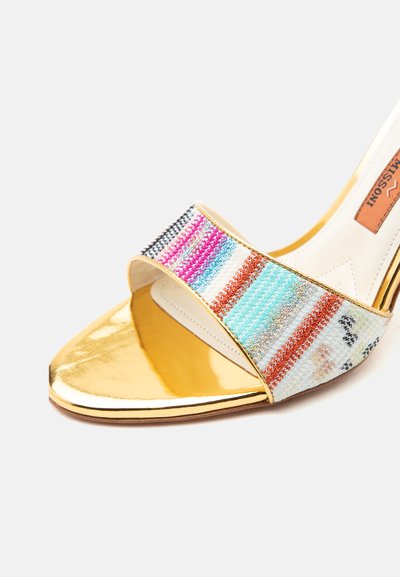 Złoty sandał na wysokim obcasie z odkrytymi palcami, z kolorowym paskiem w paski na przodzie i gładką beżową wkładką wewnętrzną.