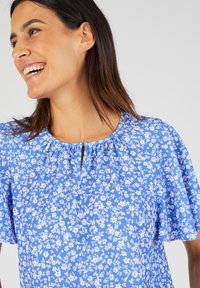 Blauwe bloemenblouse met korte, zwierige mouwen, een keyhole halslijn en een lichtgewicht stof met een wit bloemenpatroon.
