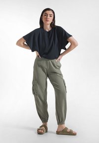 Luźna czarna koszulka zestawiona z oliwkowozielonymi spodniami cargo z bocznymi kieszeniami. Do kompletu casualowe sandały, podkreślające swobodny styl.