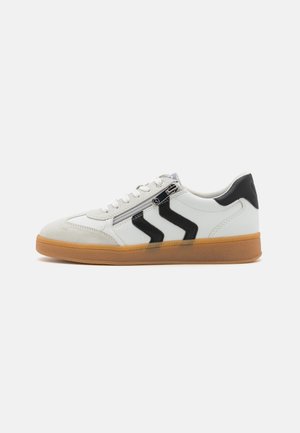 Weiße Sneaker mit schwarzen Akzenten, ausgestattet mit einer strukturierten Wildleder-Spitzkappe, seitlichen Reißverschlüssen und einer Gummisohle. Klassisches Low-Top-Design.