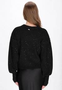 Pulover negru, tricotat, cu un design scurt, având stropi argintii, mâneci puff și margini cu tiv. Vedere din spate.