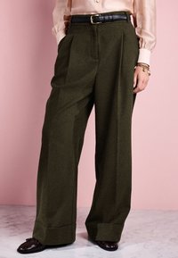 Wide-leg, high-waisted green wool trousers with pleats, finished with a cuffed hem. Paired with a black leather belt and brown loafers.