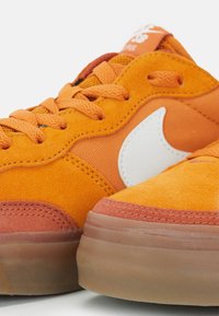 Sneaker in suede di un vivace arancione con logo bianco, dotate di accenti testurizzati e suola in gomma. Design con punta arrotondata.