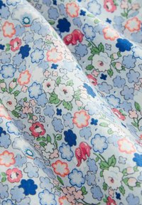Tessuto floreale con uno sfondo azzurro chiaro, caratterizzato da ciuffi di fiori rosa, rossi e bianchi, con accenti di blu chiaro e verde sparsi.