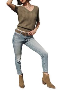 Top en tricot côtelé vert olive avec col en V, jean skinny bleu clair et bottines brunes à finition texturée avec talons blocs.