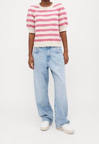Suéter de punto a rayas en rosa y crema, con mangas abullonadas y dobladillo acanalado, combinado con jeans anchos de color azul claro y zapatillas blancas.