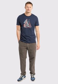 T-shirt bleu marine avec un imprimé graphique triangulaire, associé à un pantalon cargo gris avec des poches latérales et des baskets bleues.