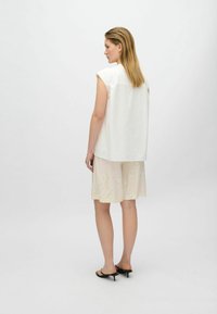 Top bianco in cotone morbido con maniche a cappuccio, abbinato a pantaloni corti beige chiaro con un motivo floreale e sandali neri con tacchi a strappy.