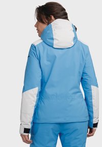 Blaue Skijacke mit strukturierten Oberflächen, weißen Akzenten an Ärmeln und Kapuze, verstellbaren Bündchen und tailliertem Design.