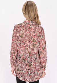 Blusa a maniche lunghe in beige con un intricato motivo paisley rosso, verde e nero; presenta un colletto a punta e polsini con bottoni.