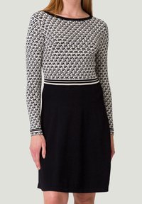 Langärmeliges Kleid mit einem Oberteil im schwarz-weißen geometrischen Muster, einem einfarbigen schwarzen Rock und einem kontrastierenden gestreiften Taillenbund. Glatte Stoffqualität.