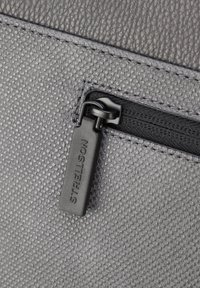 Materiale grigio testurizzato con una finitura liscia, con una zip nera e un'etichetta con la scritta "STRELSON". Dettaglio delle cuciture in primo piano visibile.