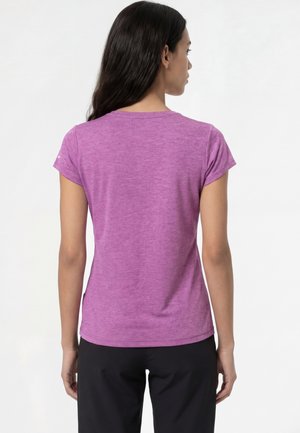 Vrouw met lang donker haar, gekleed in een aangesloten paarse T-shirt met korte mouwen en zwarte broek, van achteren gezien tegen een effen witte achtergrond.