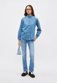 Lyseblå denimskjorte med krage, lange puffermede ermer og knappestolpe foran. Kombinert med matchende jeans og svarte platåsko, holder en liten blå veske.