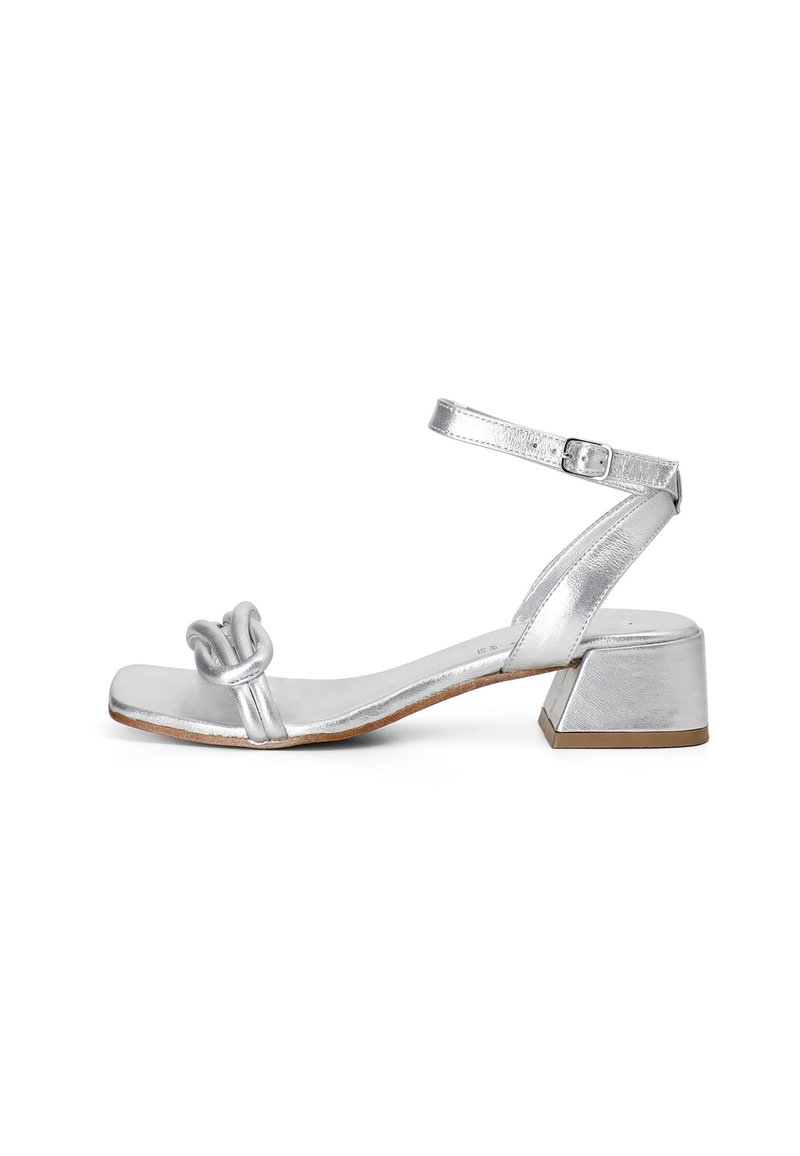 Sandal in metallo argentato con design anteriore annodato, cinturino alla caviglia regolabile e tacco quadrato, caratterizzato da una texture liscia e accenti minimi.