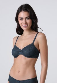Reggiseno in pizzo blu scuro con bordi smerlati, supporto con ferretto e un piccolo dettaglio a fiocco al centro. Presenta un motivo a diamante testurizzato.