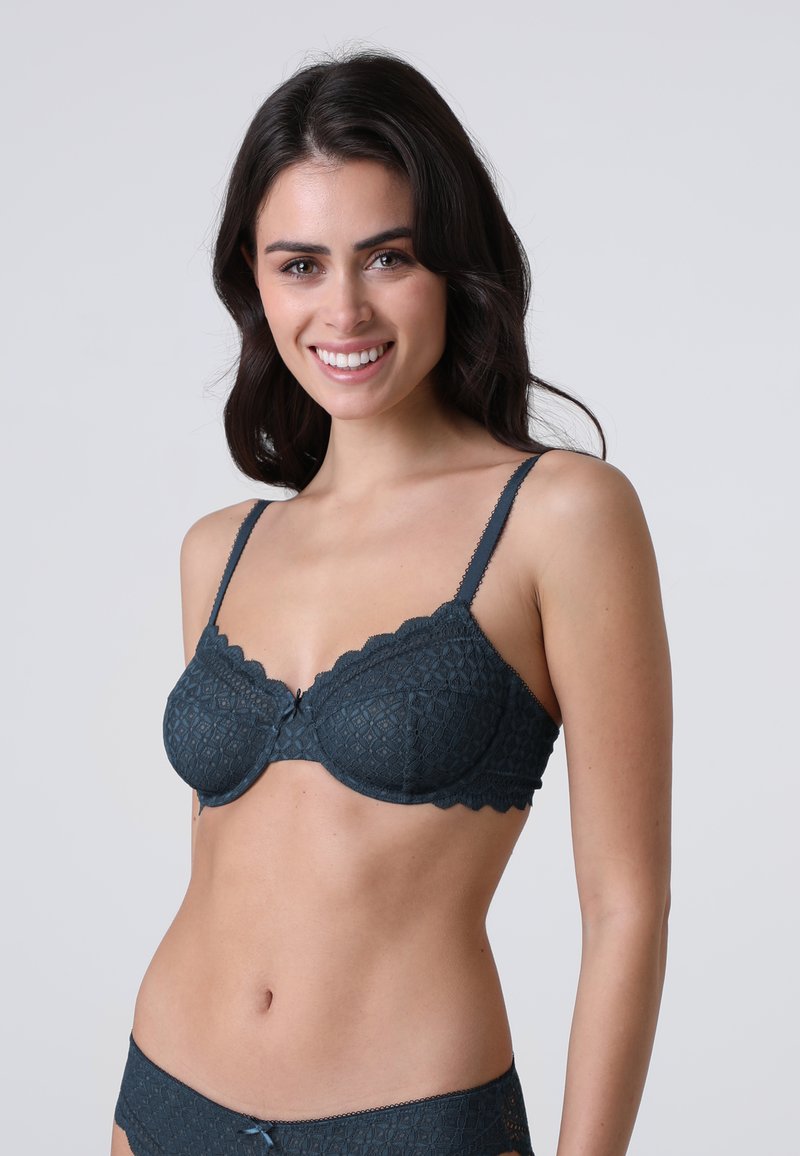 Reggiseno in pizzo blu scuro con bordi smerlati, supporto con ferretto e un piccolo dettaglio a fiocco al centro. Presenta un motivo a diamante testurizzato.