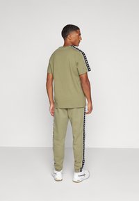 Conjunto atlético en verde olivo que presenta una camiseta de manga corta con franjas laterales negras y pantalones a juego. Tejido suave con puños elásticos.