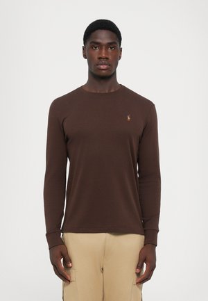 T-shirt à manches longues marron avec un col rond, fabriqué en coton doux. Présente un petit logo brodé sur la poitrine gauche et des manches ajustées.