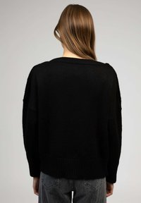 Un pull en tricot noir avec une coupe ample, un large col et un ourlet côtelé. La texture semble douce avec un style décontracté.