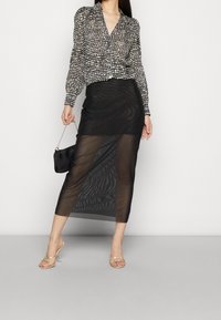 Black and white polka dot blouse with long sleeves, paired with a sheer black skirt. Features a sleek design and cross-strap heels.