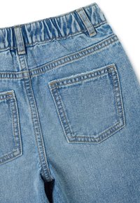 Jeans en denim bleu clair avec une taille élastique, deux poches arrière à patch et des détails de couture visibles. Texture douce avec un design classique.