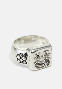 Sterlingsilverring med en fyrkantig yta prydd med ett präglat leende, accentuerad av cirkulära mönster på banden. Polerad finish.