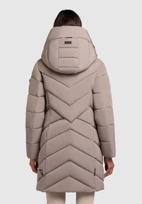 Pufjakke i lys beige med chevron-quilting, en stor hætte og sidelommer. Har et mærketag i kanten for detalje.