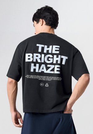 Ung mand vendt bagfra iført en sort skjorte med stor hvid tekst "THE BRIGHT HAZE" og mindre sloganskrift nedenfor på ryggen.
