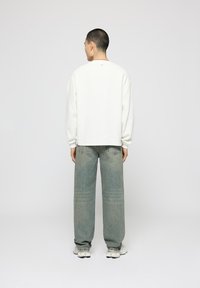 White textured long-sleeve shirt with a relaxed fit, paired with light blue loose-fit jeans, worn with modern sneakers.