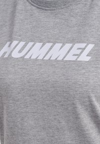 Grauer Stoff mit dem Markennamen "HUMMEL", groß und fett in weißen Buchstaben über der Brust gedruckt.