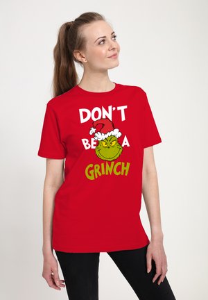 Červené bavlněné tričko s krátkým rukávem, na kterém je zelená grafika Grinče v santovské čepici a bílý text "NEBUĎ GRINČEM."