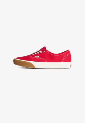 Zapatillas bajas de lona roja con suelas de goma blancas, diseño con cordones y detalles marrones en la punta. Etiqueta con el logo visible en el costado.