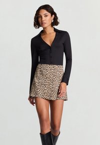 Schwarzes langärmliges Hemd mit Knopfverschluss am Ausschnitt, kombiniert mit einem Minirock in Leopardenmuster. Das Modell trägt kniehohe schwarze Stiefel.