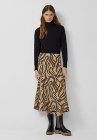 Schwarzer Rollkragenpullover mit langen Ärmeln, kombiniert mit einem knielangen beigen Rock mit einem braunen abstrakten Muster. Schwarze ankle boots mit dicken Sohlen.